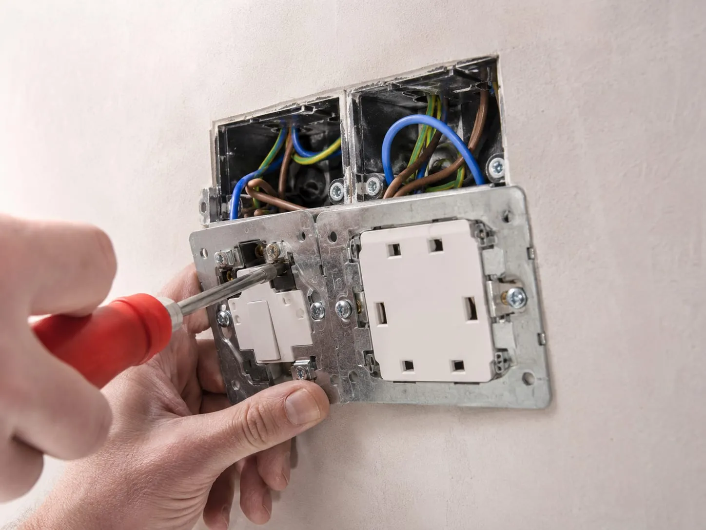 Close-up of an electrician fitting a new double socket and switch, wiring visible in the back box